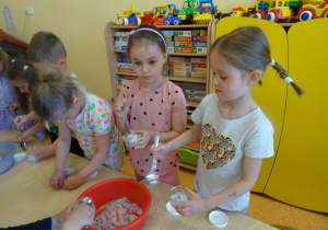 Dzieci nasypują łyżkami mieszankę soli z płatkami kwiatów do pojemników.